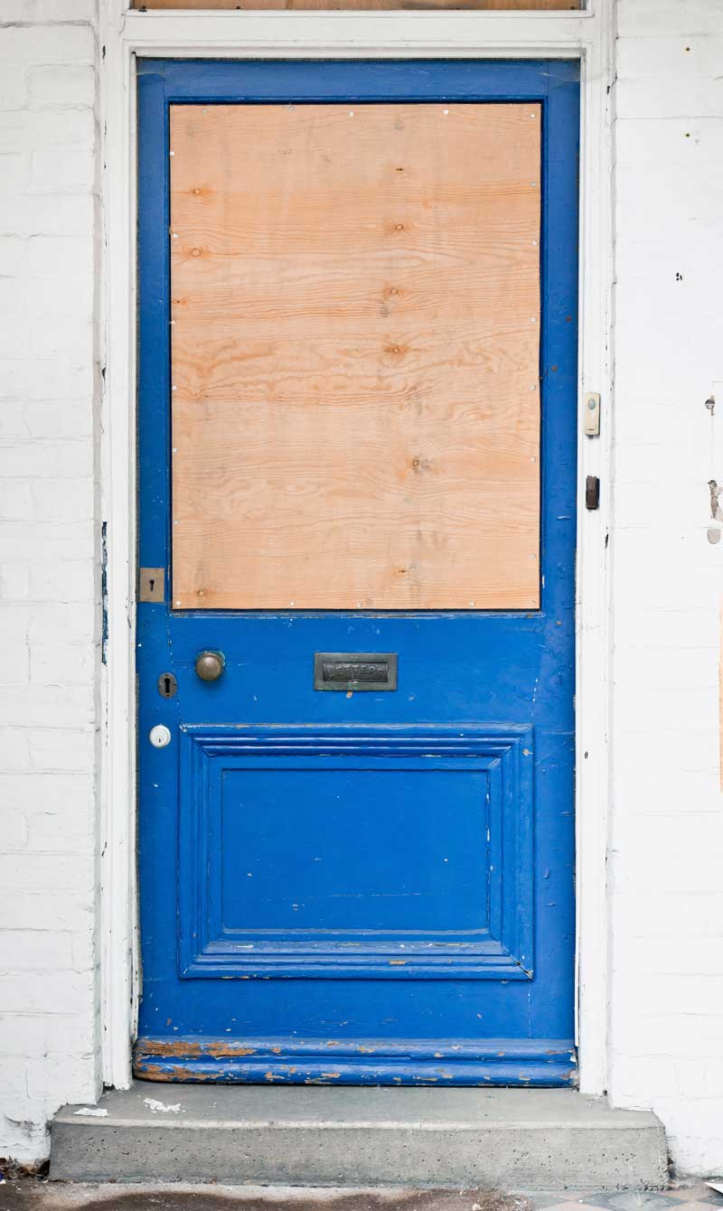 Front door with plywood board covering glass